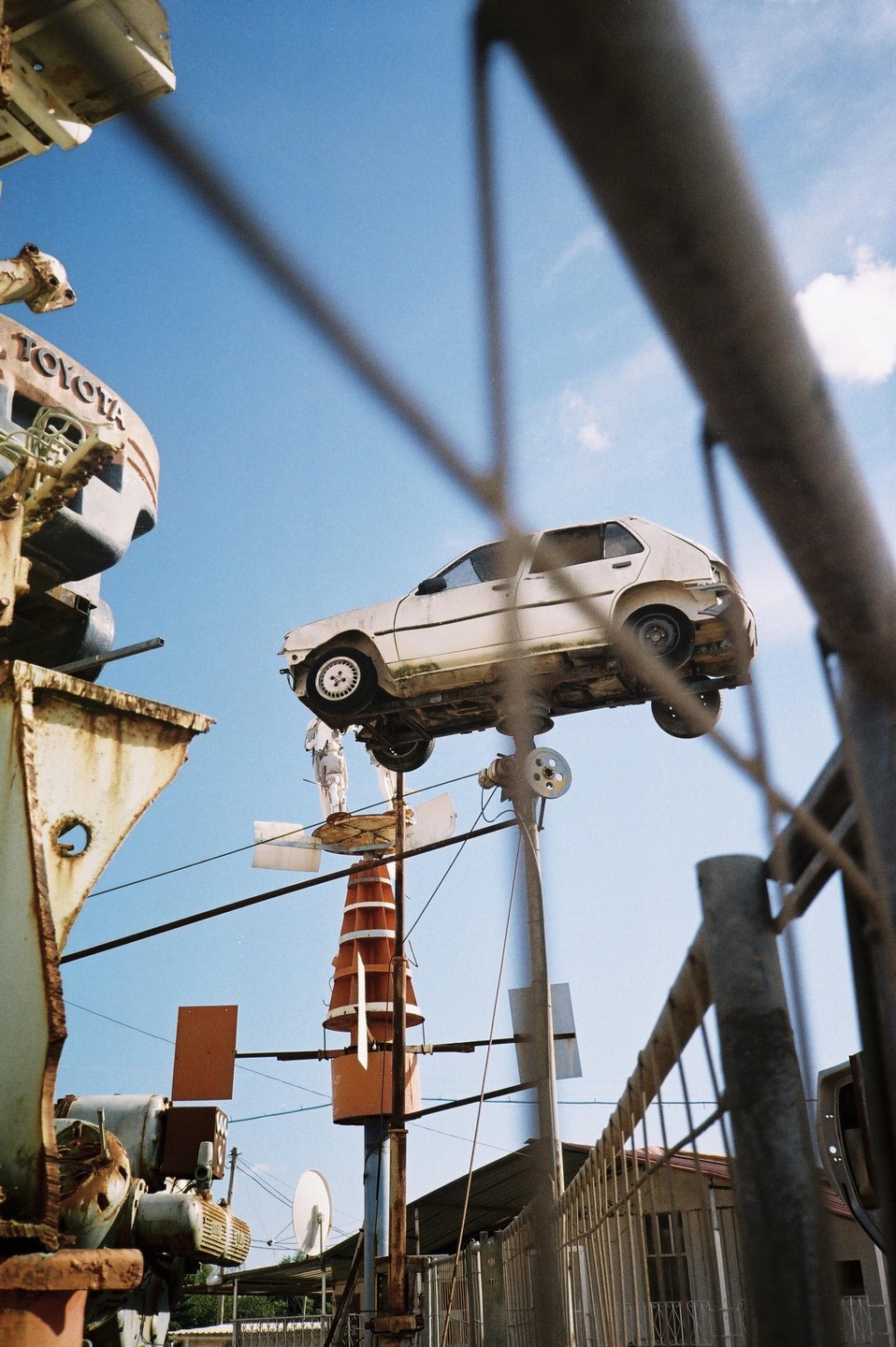 A white car is mounted on a tall pole next to other metal structures under a clear blue sky.