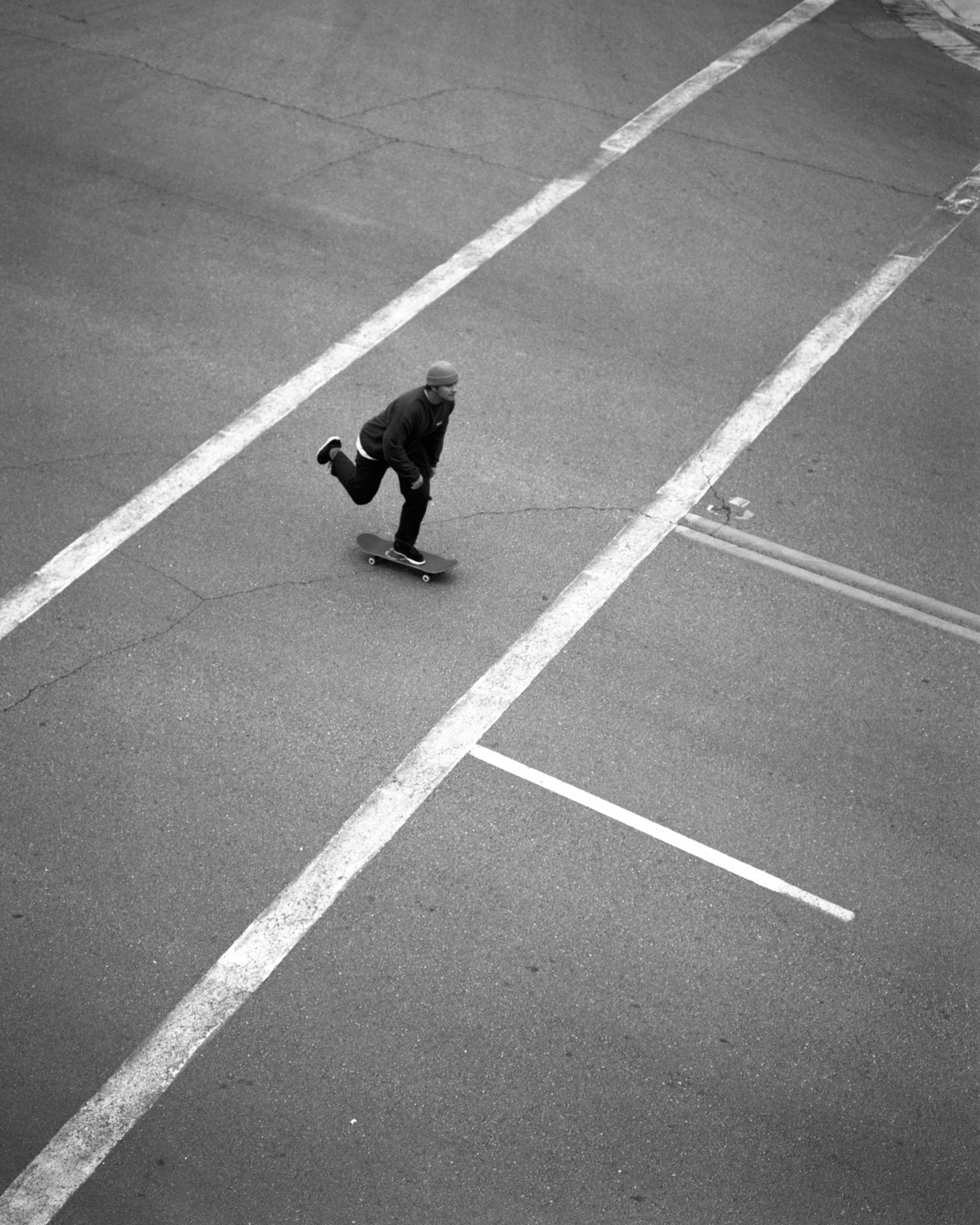A man on a skateboard pushes himself along an empty street marked with white lines.