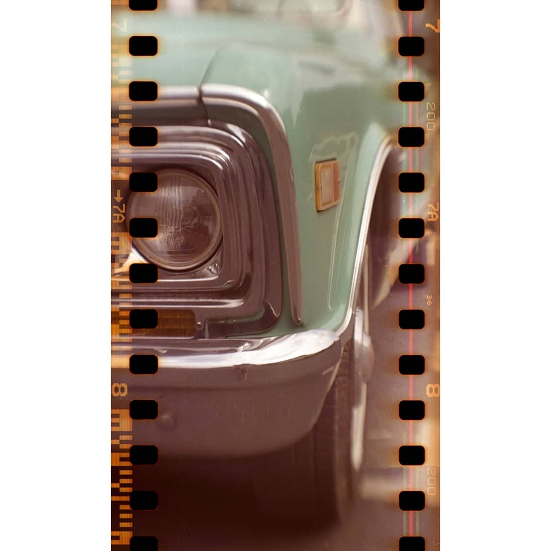 The front of a light green truck with a chrome bumper and headlight is visible through a film strip.