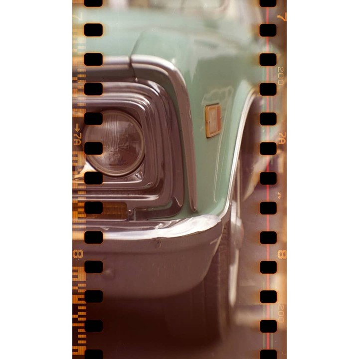 The front of a light green truck with a chrome bumper and headlight is visible through a film strip.