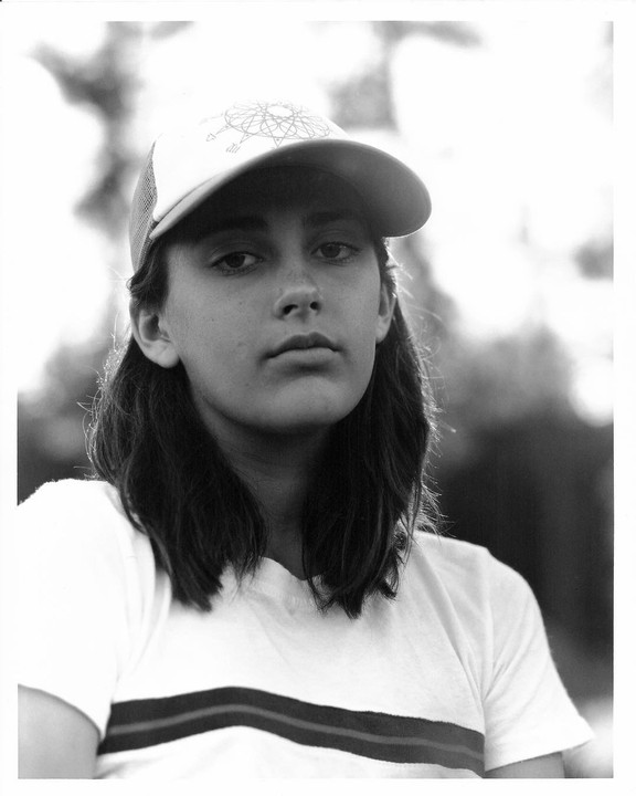 A young woman wearing a baseball cap and a striped t-shirt looks directly at the viewer.