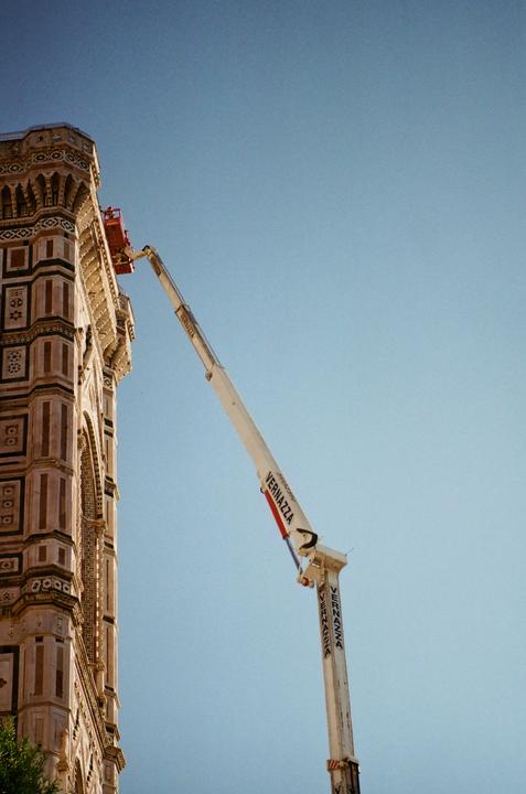 A construction crane extends towards the top of a building with intricate architectural details under a clear sky.