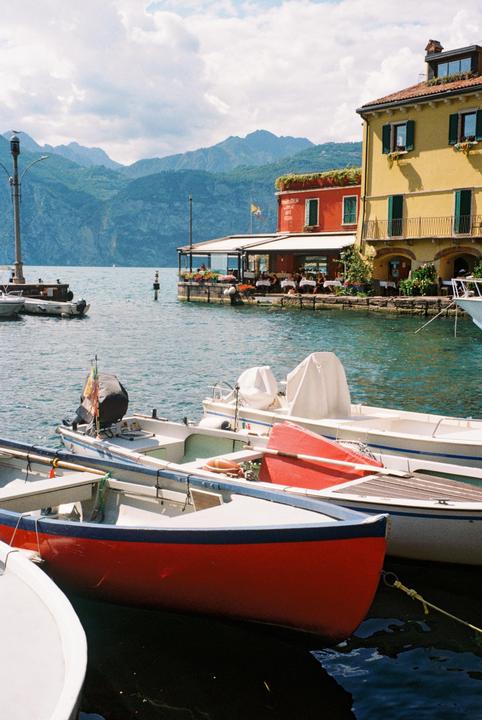 Several boats are moored in a harbor with colorful buildings and mountains in the background.