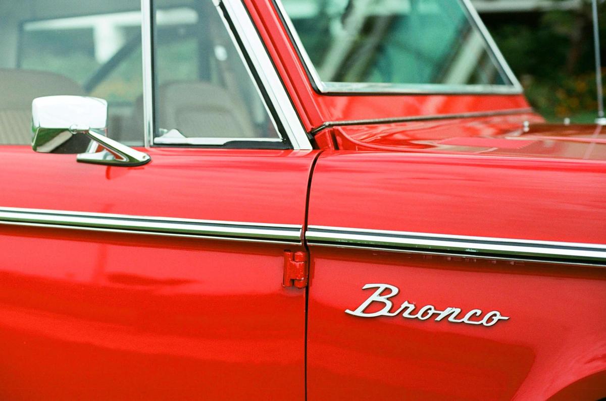 A red Bronco is visible from the side, showing the door, window, and side mirror.