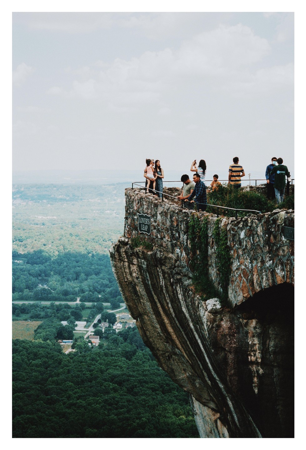 A group of people stand on a stone overlook called Lover's Leap, high above a valley filled with trees and a small town.