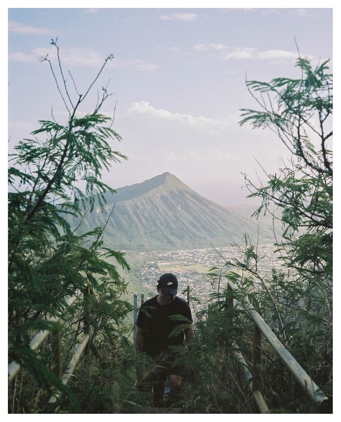 A man climbs stairs on a mountain path overlooking a town and another mountain.