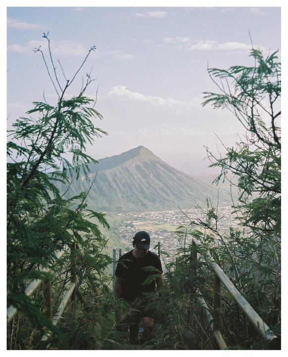 A man climbs stairs on a mountain path overlooking a town and another mountain.