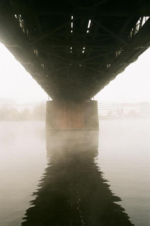 A bridge spans a body of water, with its underside and a support pillar reflected in the misty surface.