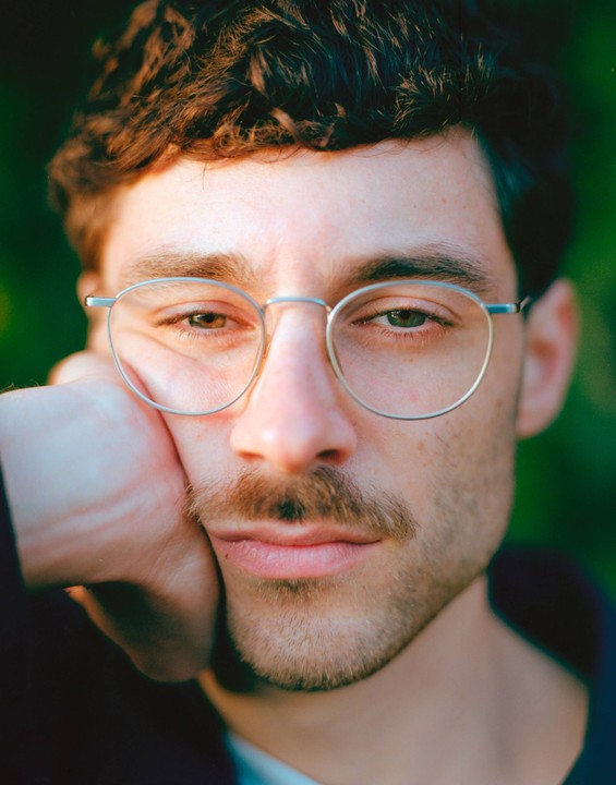 A man with glasses and a mustache rests his head on his hand.