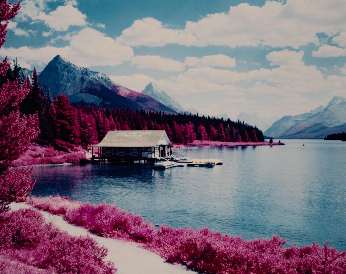 A boathouse sits on the shore of Maligne Lake, surrounded by mountains and trees.