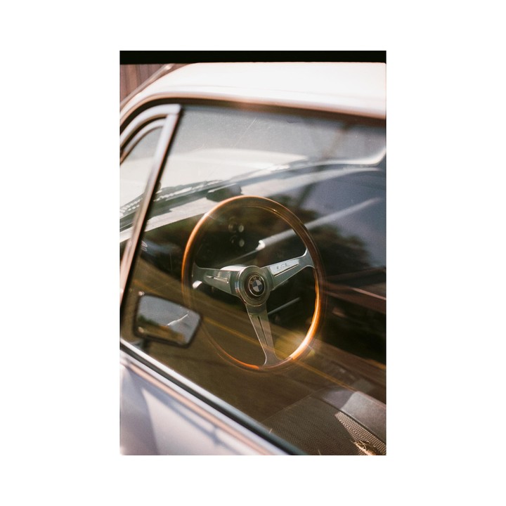A wooden steering wheel with a BMW logo is visible through the window of a car.