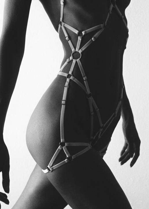 A woman's torso and legs are visible, adorned with a harness.