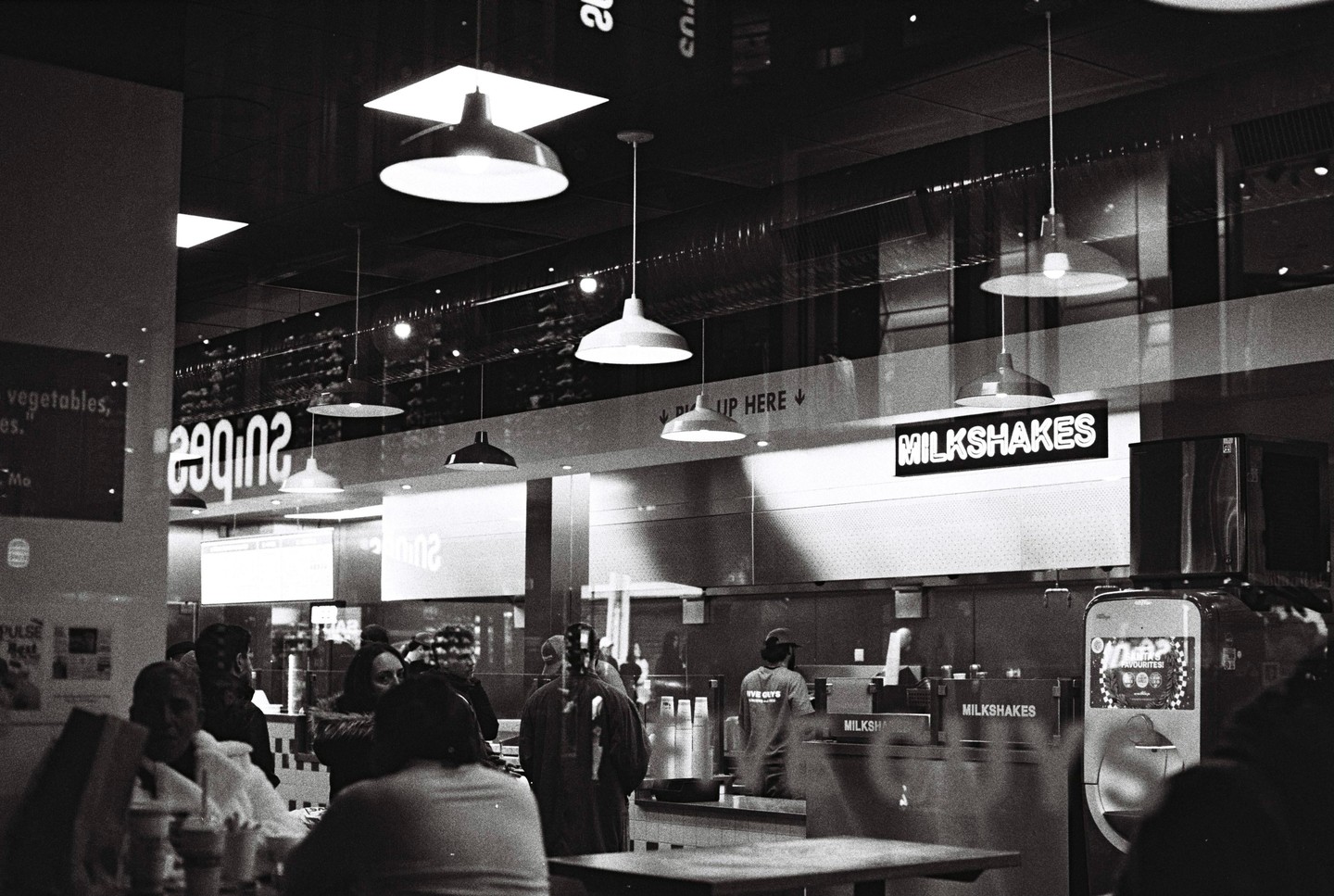 People are gathered inside a restaurant with a "Milkshakes" sign visible above the counter.