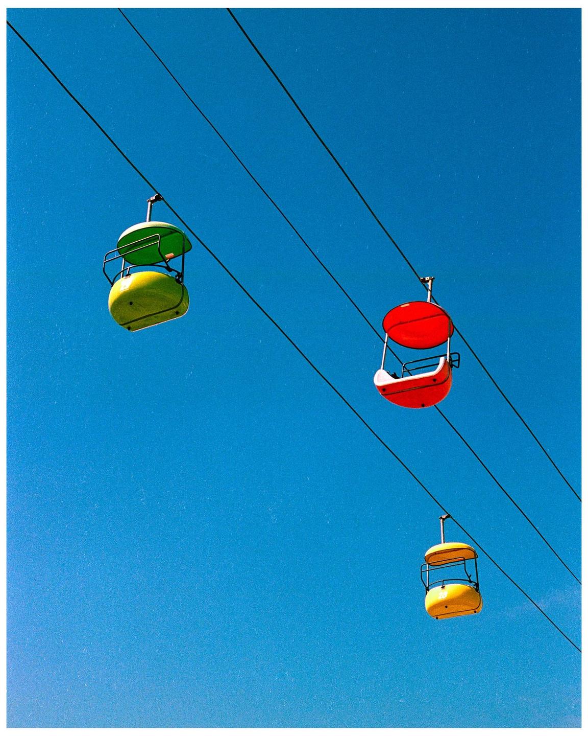 Three colorful gondolas are suspended by cables against a clear blue sky.