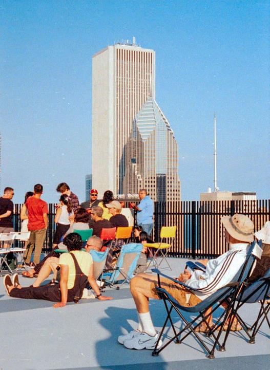 A group of people are gathered on a rooftop with city buildings in the background.