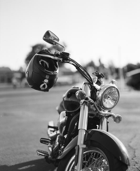 A motorcycle with a helmet hanging from its handlebar is parked on a paved surface.