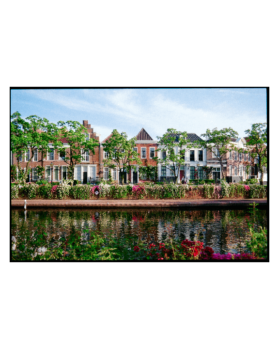 A row of houses with flowering plants along a canal is visible under a blue sky.