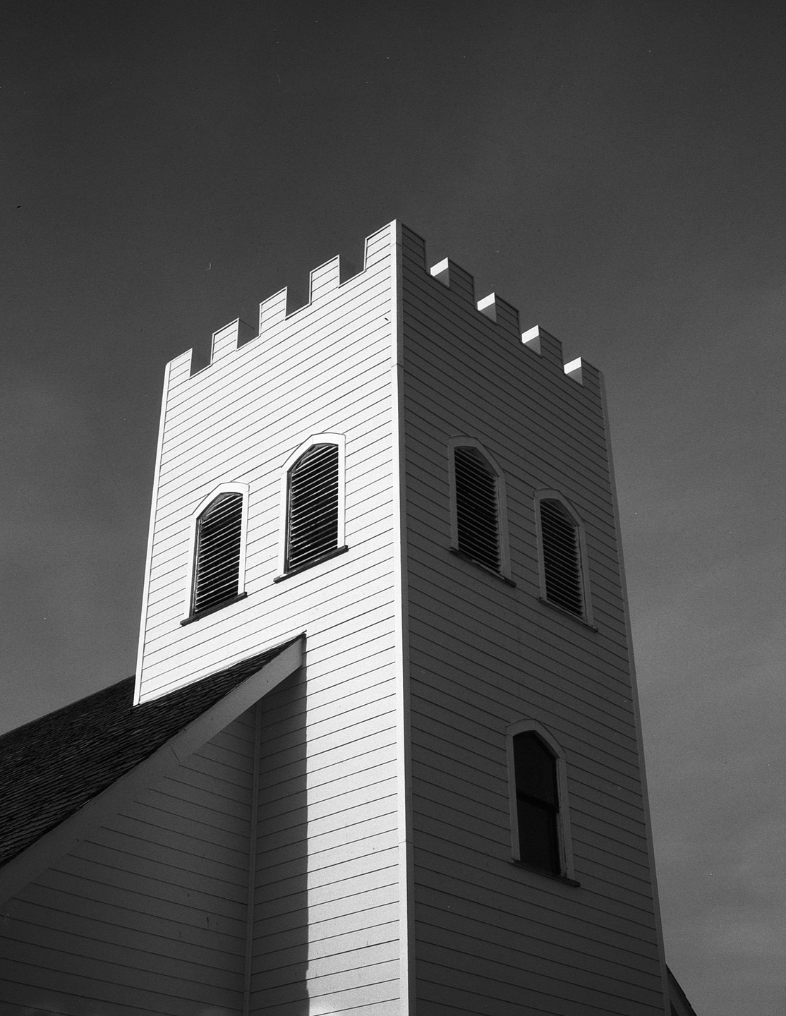 A tall, white church tower with arched windows stands against a dark sky.