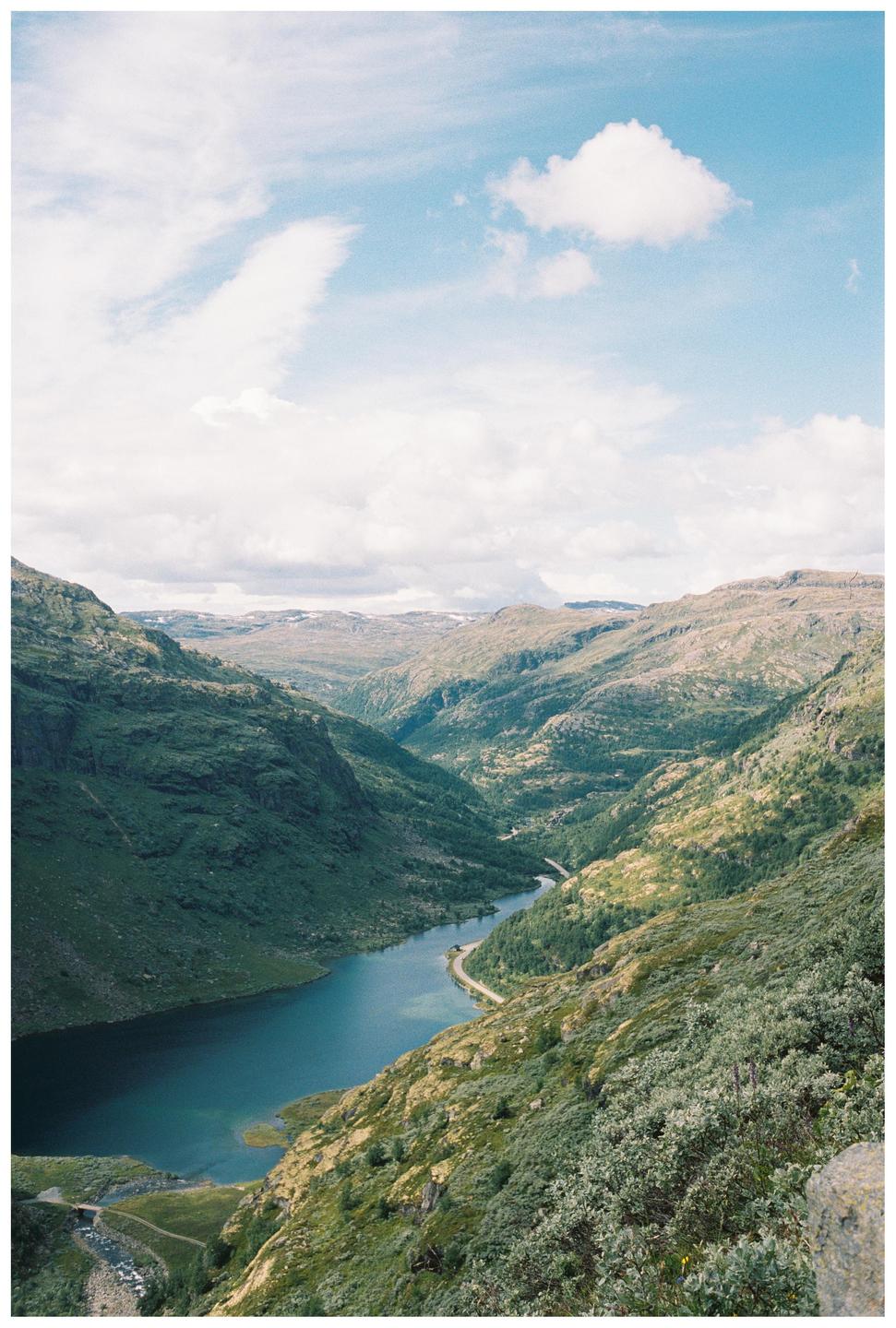 A winding river flows through a valley surrounded by mountains under a cloudy sky.