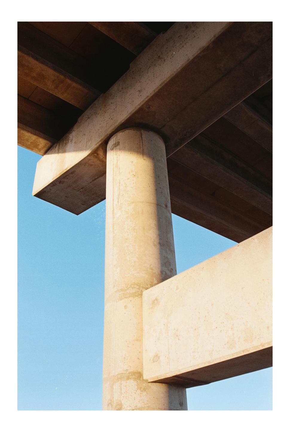 A concrete pillar and beams are visible against a clear blue sky.