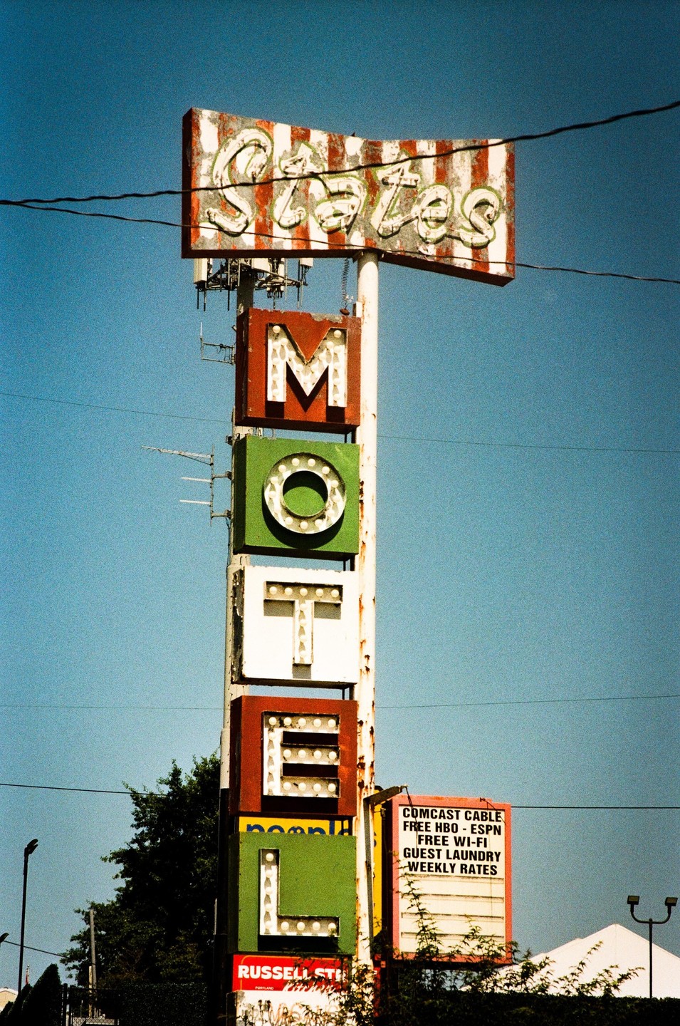 A tall, weathered motel sign with colorful letters stands against a clear blue sky.
