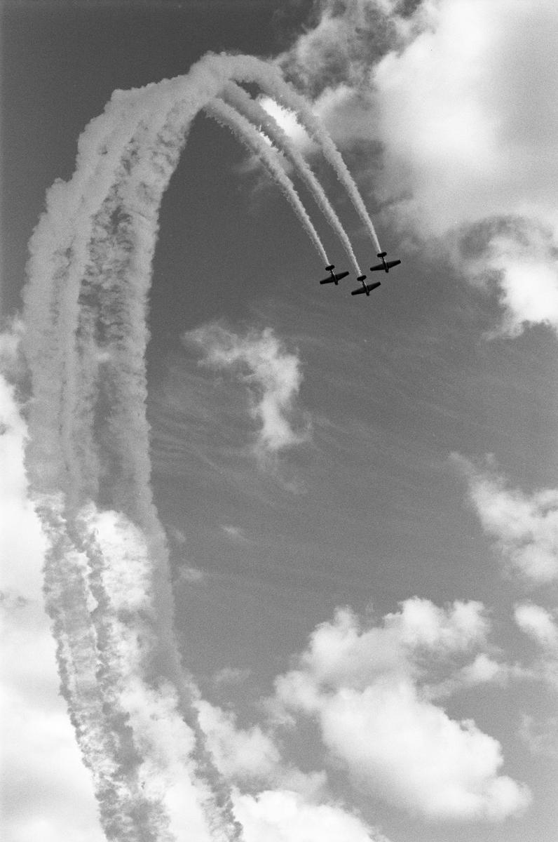 Three airplanes fly in formation, leaving smoke trails that curve downwards against a cloudy sky.