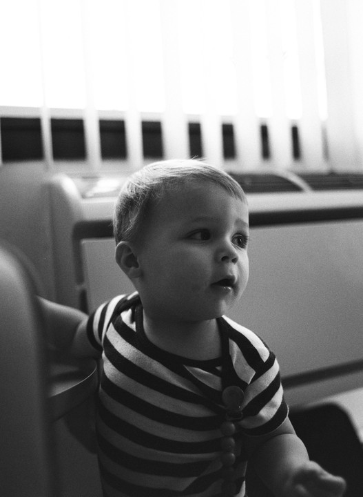 A child in a striped shirt looks to the right with a window and blinds in the background.