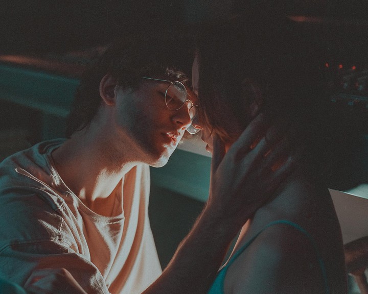 A man wearing glasses leans in to kiss a woman, with his hand gently touching her neck.