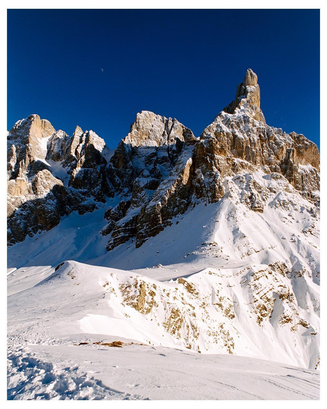 A snow-covered mountain range with a clear blue sky and a crescent moon is visible.