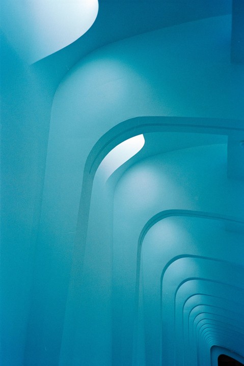 A series of blue arches recede into the distance, with light sources visible within some of the arches.