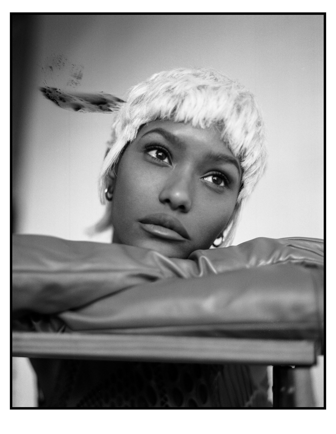 A woman with short, light-colored hair rests her arms on a surface, looking upwards.