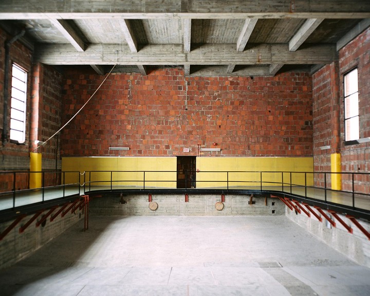An empty indoor swimming pool with a yellow wall and brick walls is visible.