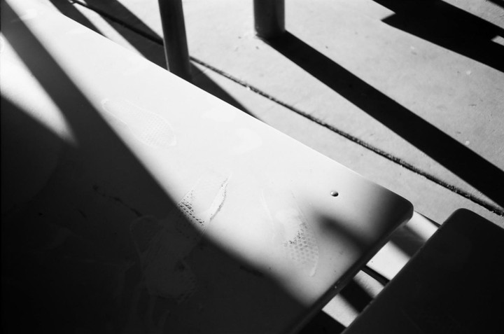 Sunlight casts strong shadows across a white surface with faint shoe prints.