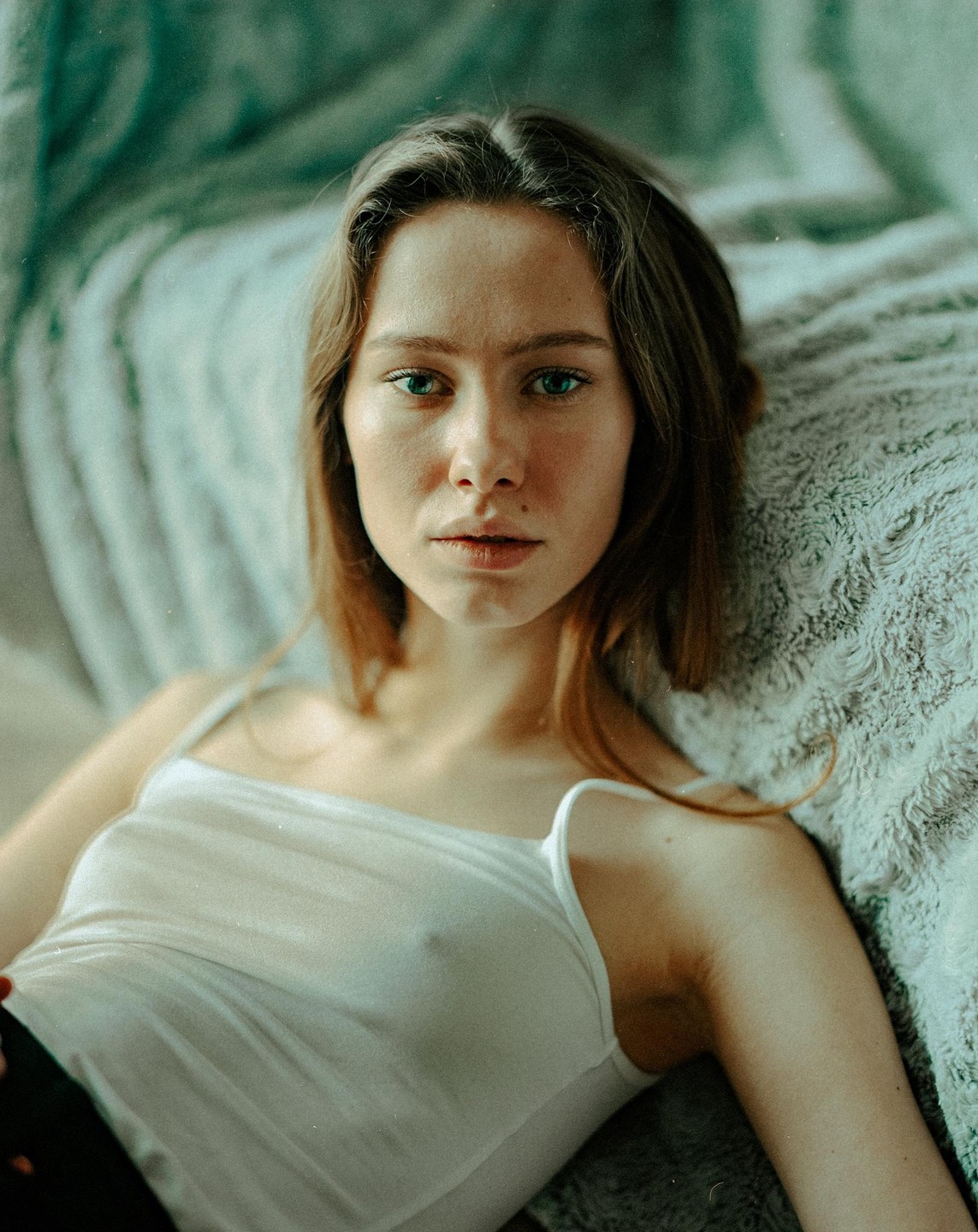 A woman with long hair and a white tank top is lying on a textured blanket.