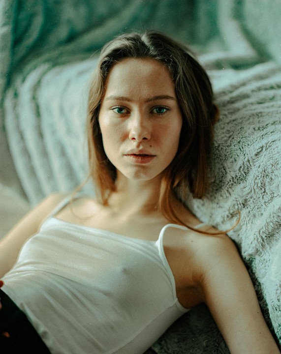 A woman with long hair and a white tank top is lying on a textured blanket.