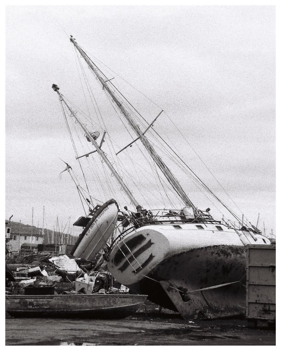 A large sailboat with two masts is beached and leaning to one side, with a smaller boat hanging from its side.