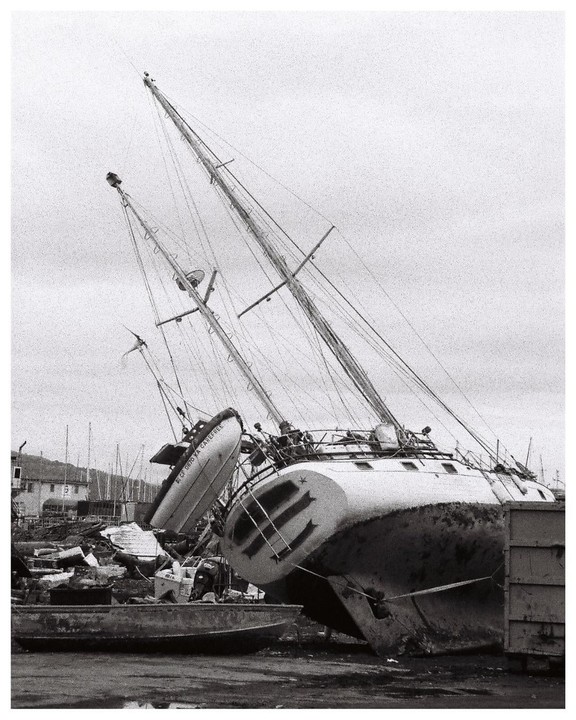 A large sailboat with two masts is beached and leaning to one side, with a smaller boat hanging from its side.