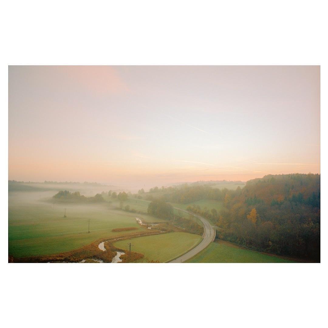 A winding road and river cut through a misty, green valley at dawn, with a forest on the right.