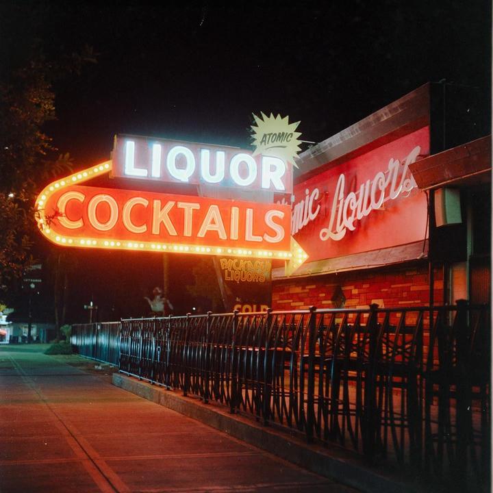 A neon sign for liquor and cocktails illuminates a building at night.