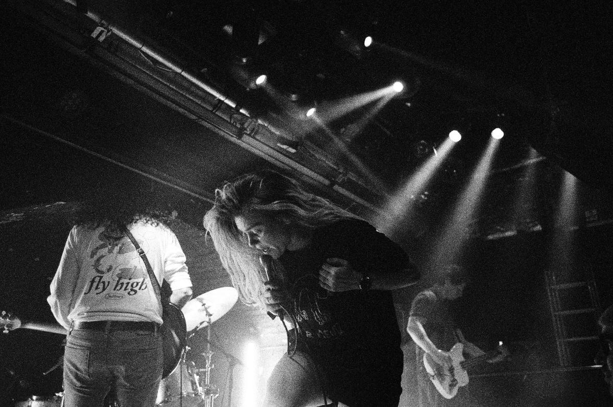 A woman sings into a microphone on a stage with other musicians and bright spotlights.