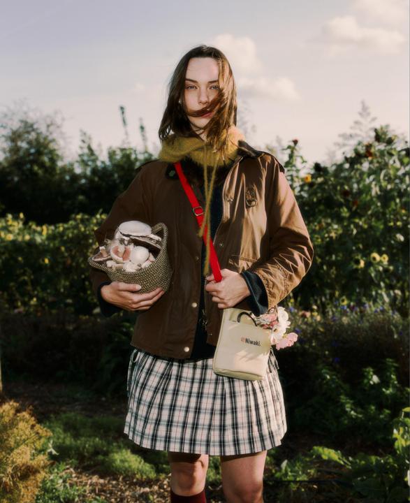 A woman stands in a garden holding a basket of mushrooms and a small bag with flowers.