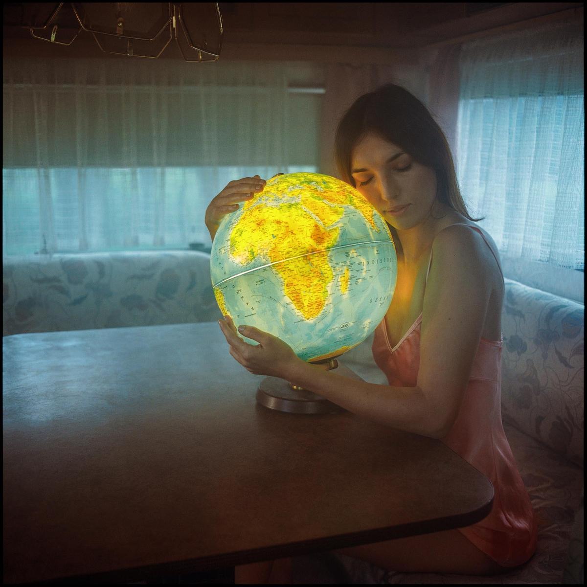 A woman in a pink dress embraces a glowing globe in a dimly lit room.