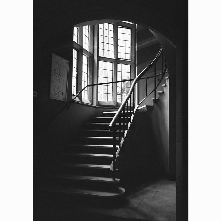A grand staircase with a curved railing leads up to a large window with many panes.