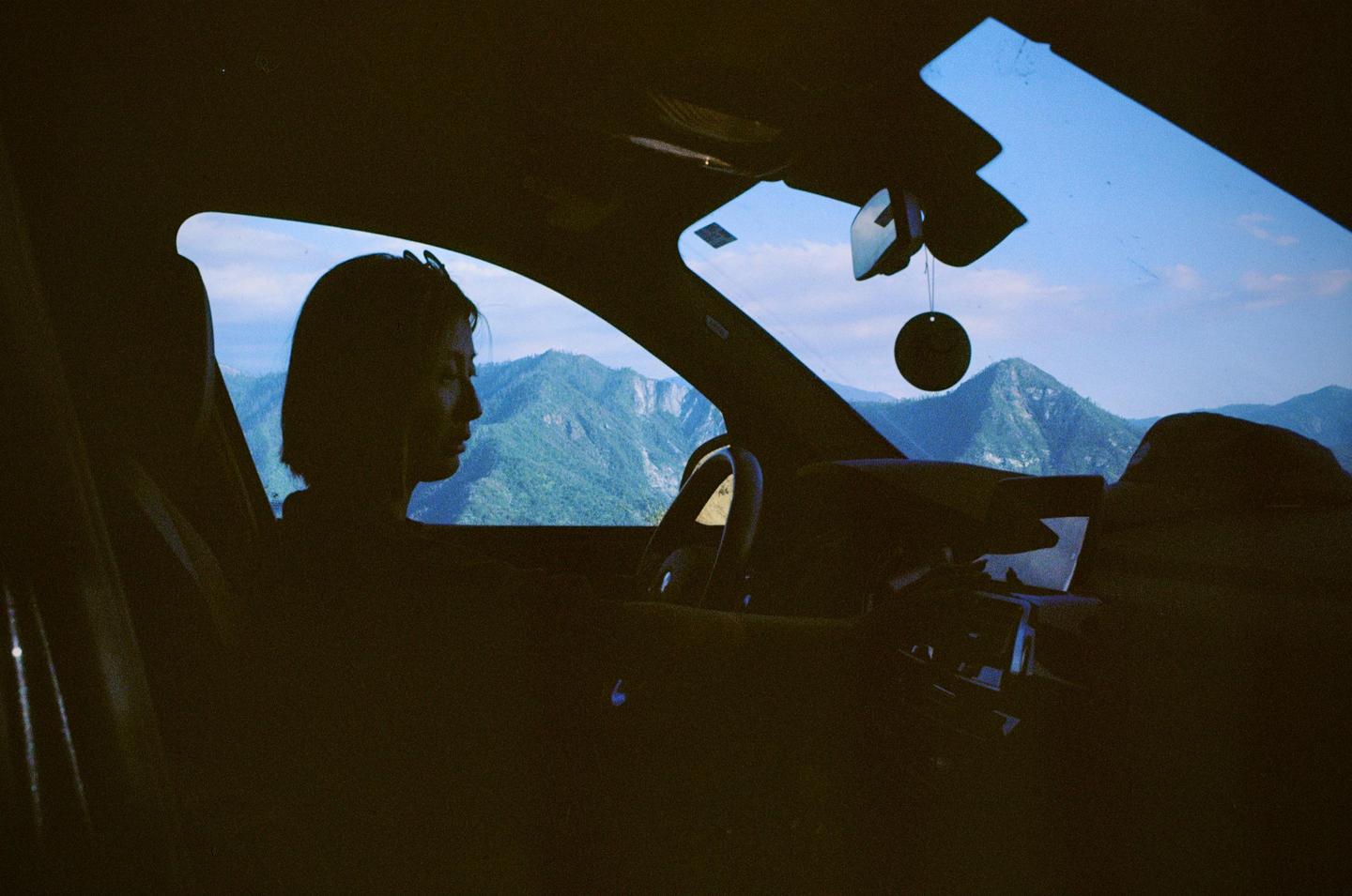 A woman sits in a car looking out at a mountain landscape.