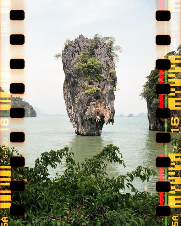A large rock formation covered in trees rises from the water, with other islands visible in the distance.