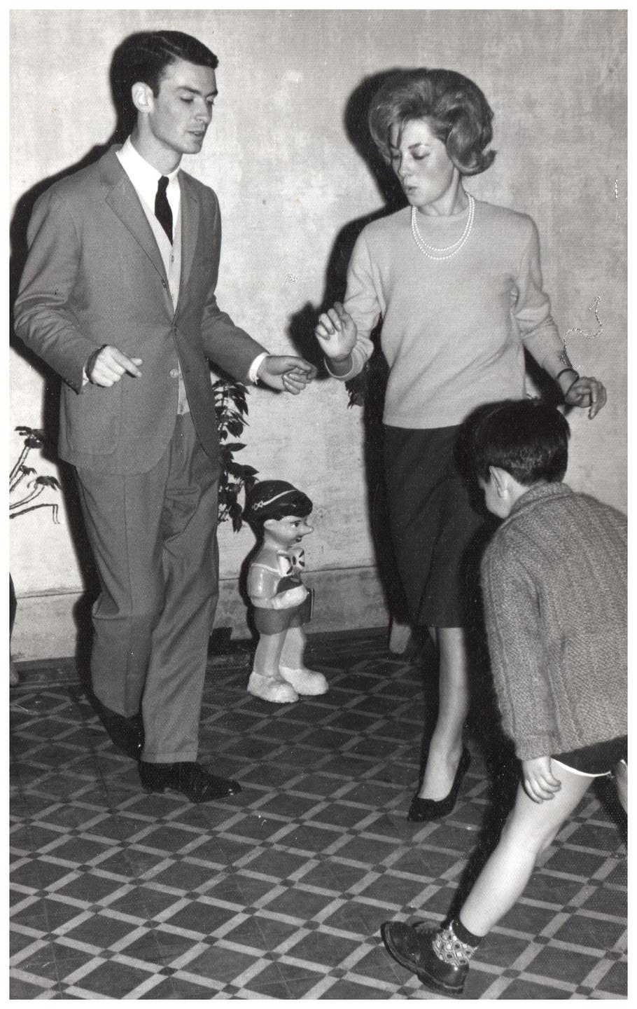 A man, a woman, and a child are dancing on a tiled floor next to a Pinocchio doll.