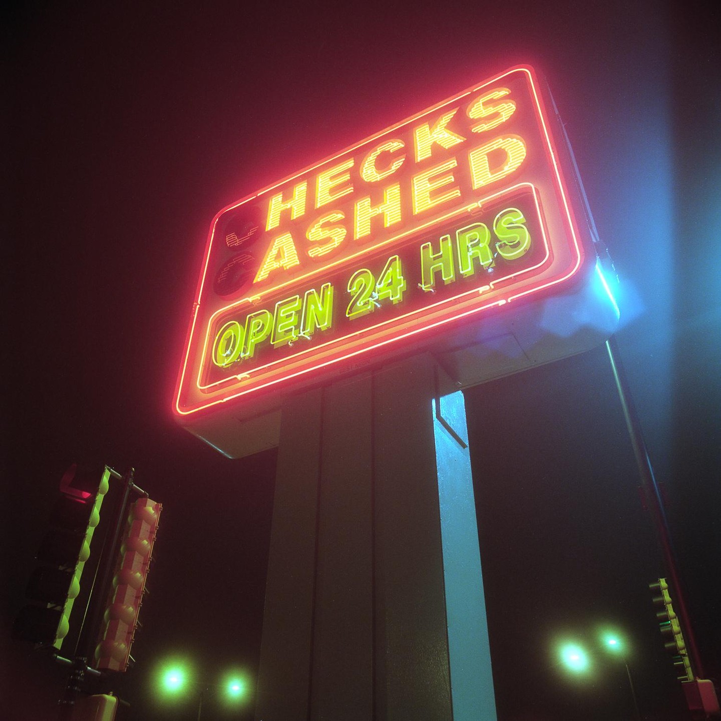 A neon sign for "Hecks Ashed Open 24 Hrs" glows brightly against a dark night sky.