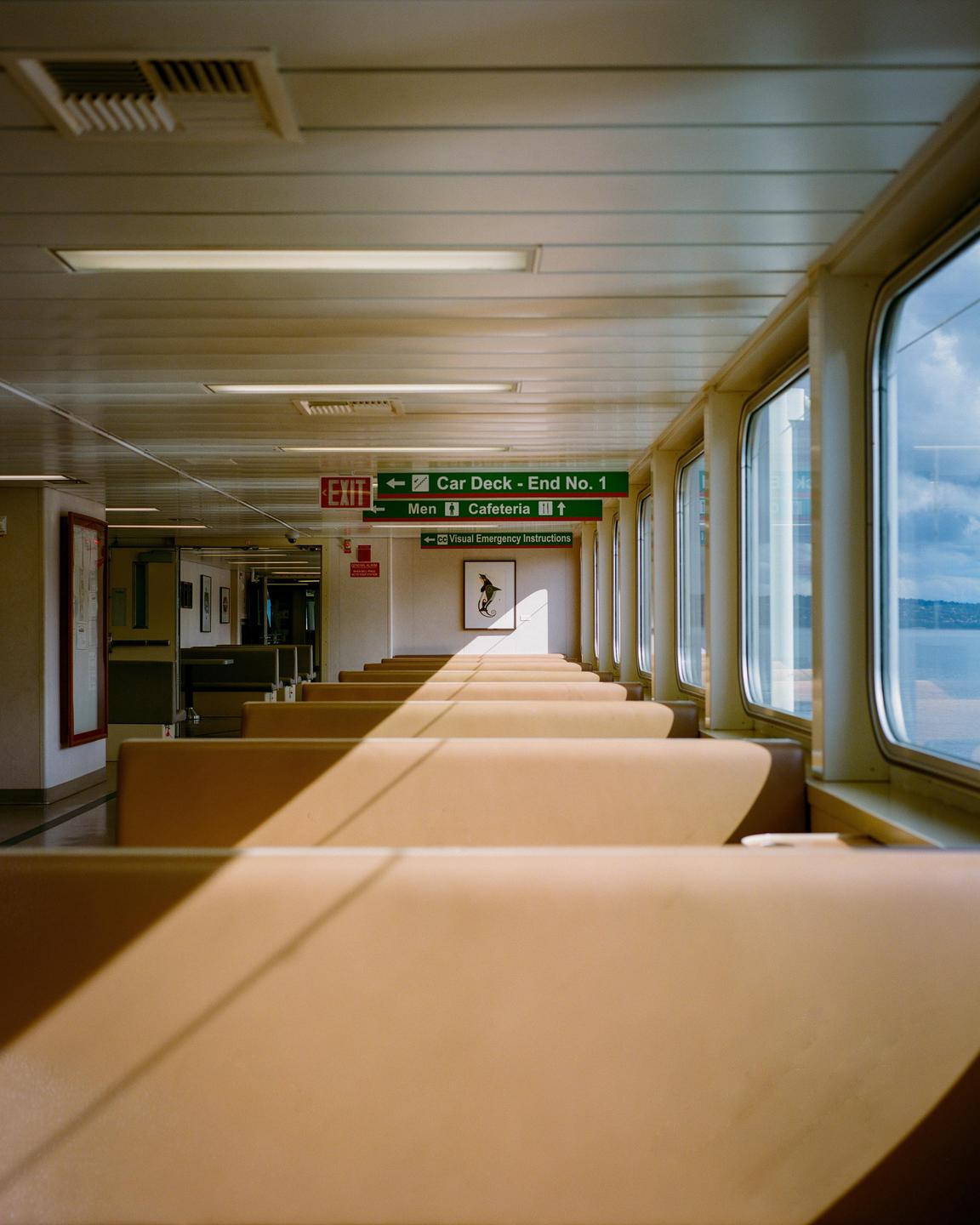 A long row of empty seats on a ferry boat is illuminated by strong diagonal sunlight from the windows.