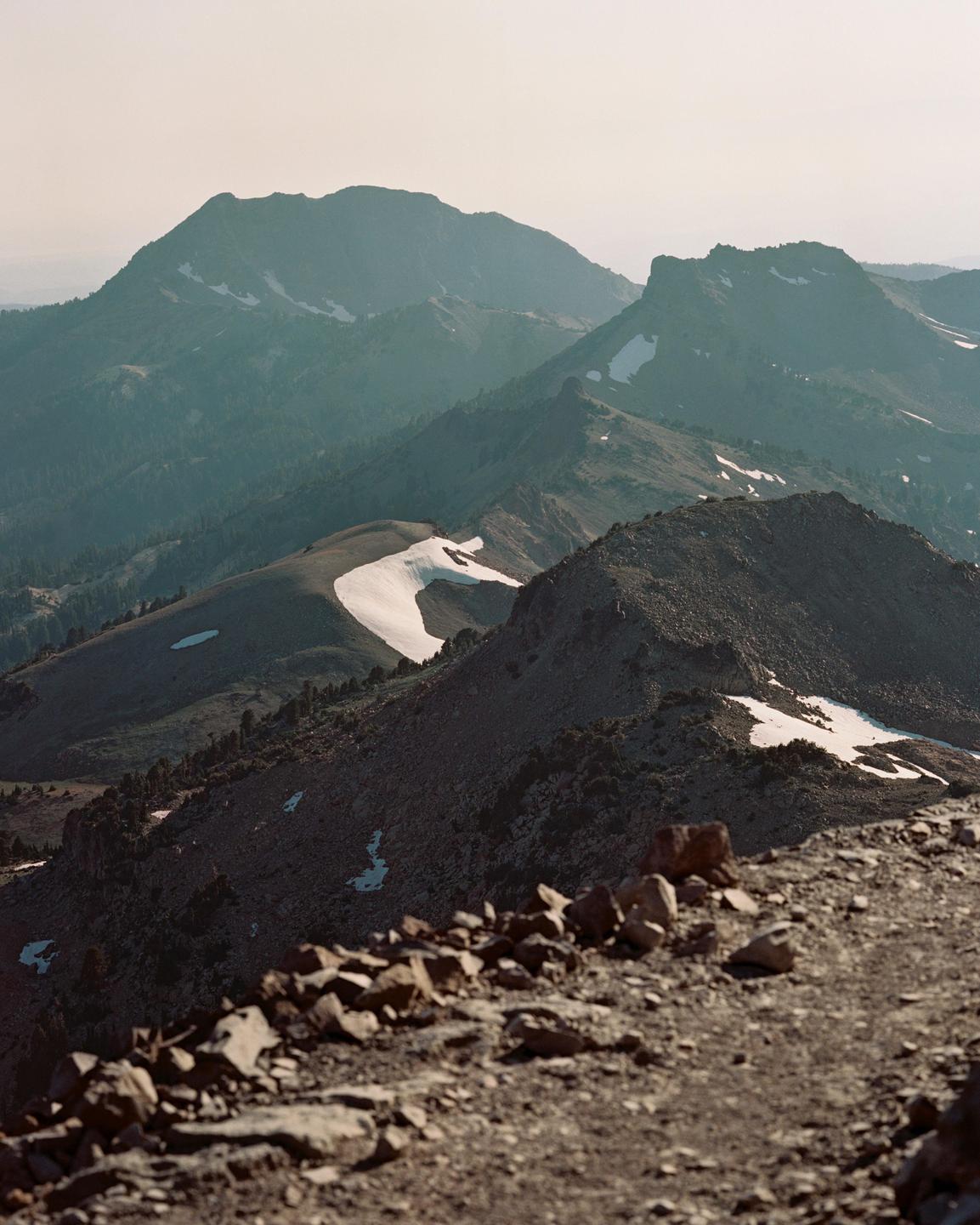 A mountain range with patches of snow is visible from a rocky foreground.