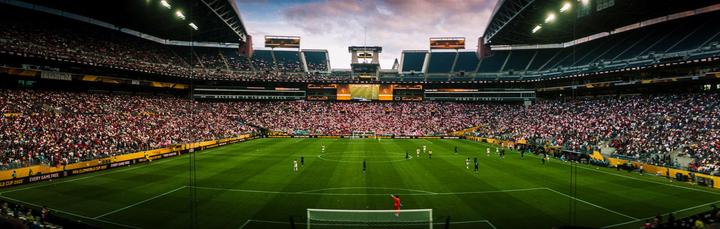 A wide shot shows a soccer match in progress at a stadium filled with spectators.